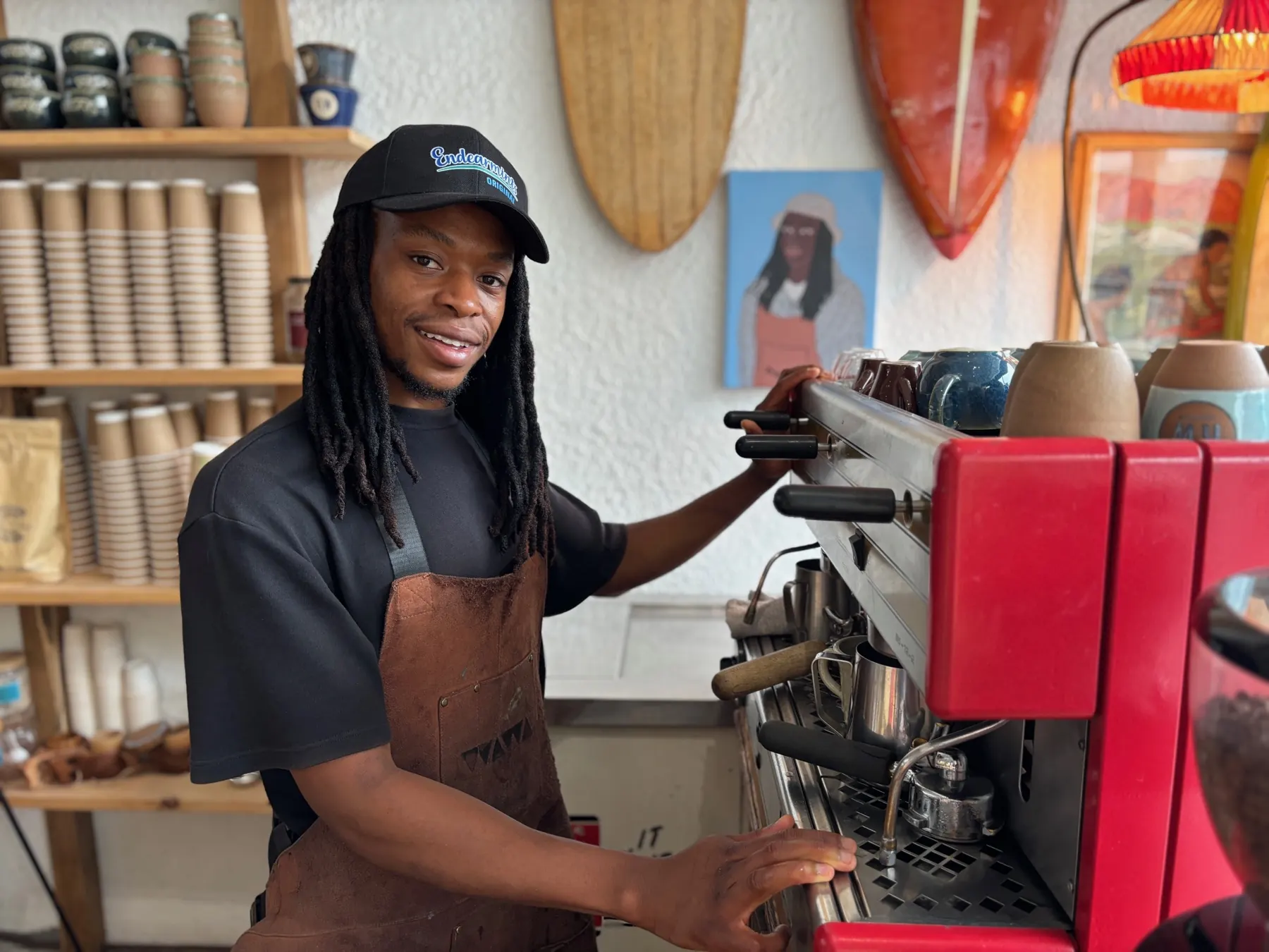 Barista pulling a shot on the red espresso machine, boards on the wall behind