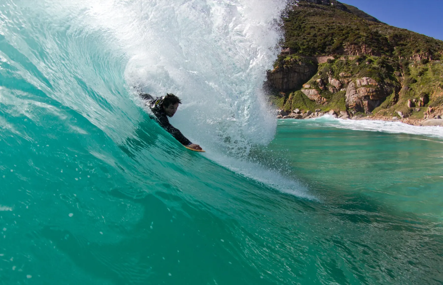 A bodysurfer deep inside a teal barrel on a handplane