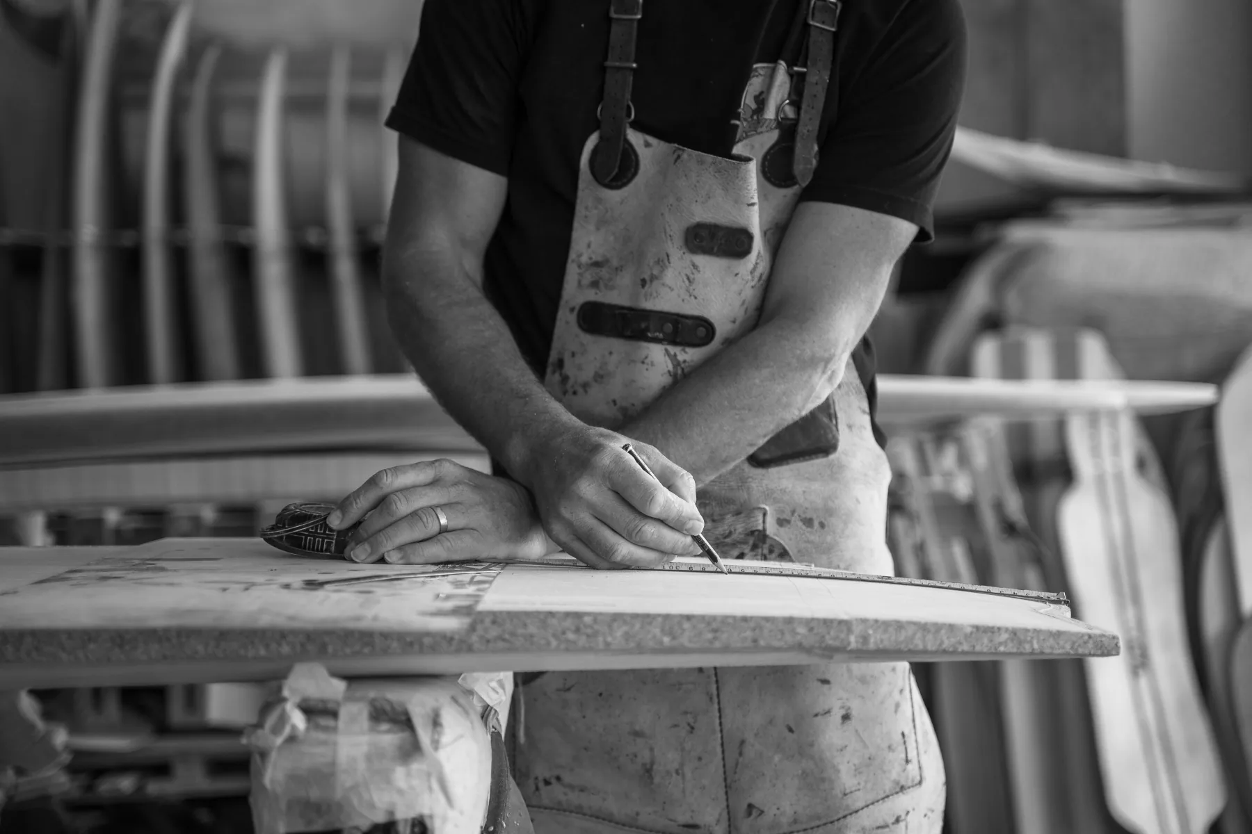 A shaper in a stained apron marking an outline on a blank with a pencil and steel rule